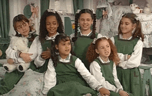 a group of young girls wearing green overalls and white shirts are posing for a picture