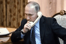 a man in a suit and tie is sitting at a desk talking on a telephone .