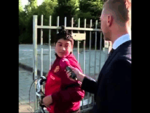 a man in a suit is talking to a boy wearing a red jacket that says manchester united