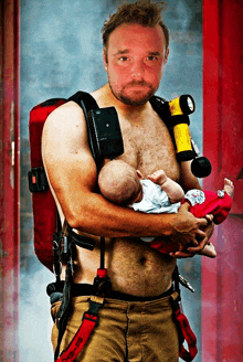 a shirtless fireman holds a baby in his arms with a red belt that says rescue