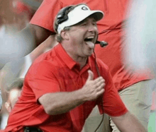 a man wearing a red shirt and a white hat with the letter g on it is laughing with his tongue out .