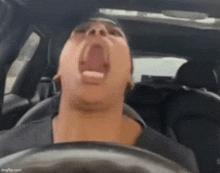 a man is yawning while driving a car .