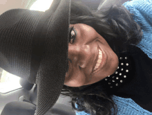 a woman wearing a black hat and a blue sweater smiles for the camera