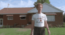 a man is standing in front of a brick house wearing a t-shirt that says ' a ' on it