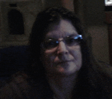 a woman wearing glasses is looking at the camera in a dark room