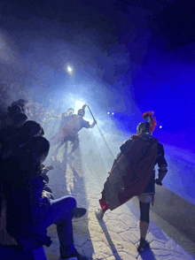 a man in a red cape and helmet holds a sword in front of a crowd of people