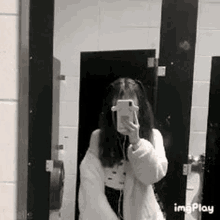 a woman is taking a selfie in a public restroom with her phone .