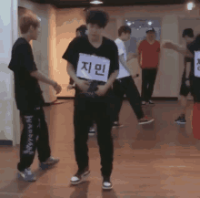 a group of young men are dancing in a room with one wearing a sign that says " 지민 " on it