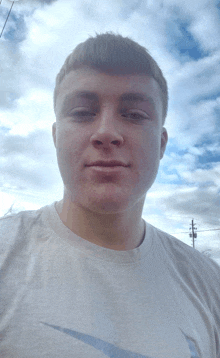 a young man wearing a nike shirt takes a selfie in front of a cloudy sky