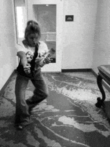 a black and white photo of a woman playing a guitar in a hallway with a sign on the wall that says 924