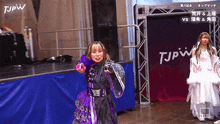 a woman in a purple dress is standing on a stage in front of a sign that says tjpw .