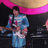 a man in a blue uniform plays a guitar in front of a vox amplifier