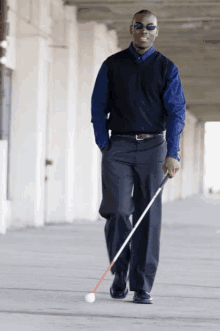 a man wearing sunglasses and a blue shirt is walking with a cane