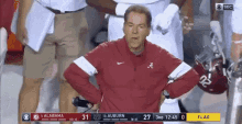 a man in a red jacket with the letter a on it is watching a football game between alabama and auburn .