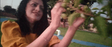 a woman in a yellow dress is picking fruit from a tree branch .