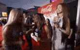 a group of women are standing next to each other on a red carpet in front of a coca-cola sign .