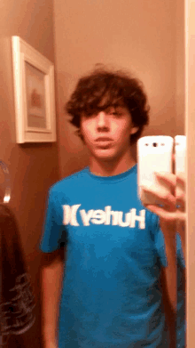 a boy taking a picture of himself in a mirror wearing a blue shirt that says vehuh