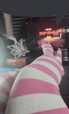 a person wearing pink and white striped socks sits in front of a computer screen that says scp-049-2