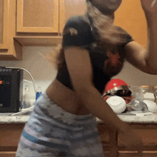 a woman in a crop top and shorts is dancing in a kitchen with a microwave in the background .