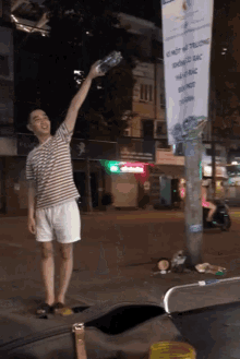 a man holds up a bottle of water in front of a sign that says " no smoking " on it