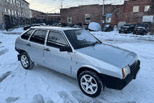 a silver car is parked in a snowy lot in front of a brick building