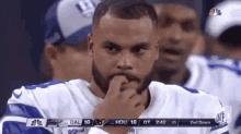 a man with a beard is sitting on the sidelines of a football game with his hand on his chin .