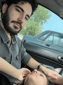 a man with a beard sits next to a woman in a car with her eyes closed