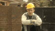 a man wearing a yellow hard hat is sitting in front of a brick wall with his arms crossed .