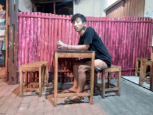 a man sits at a table in front of a pink fence with a sign that says ' coca cola ' on it