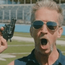 a man wearing sunglasses is holding a gun in his hand and shouting .