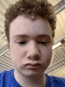 a young man with curly hair is wearing a blue t-shirt and making a funny face .