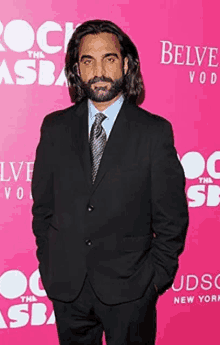 a man in a suit and tie stands in front of a pink wall that says belvedere