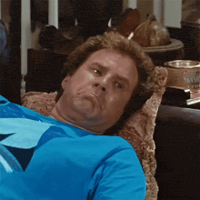 a man in a blue shirt is laying on a couch and making a face .