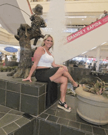 a woman sits in front of a statue of a boy with a fishing rod and a sign that says grande y rapida