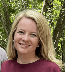 a woman wearing a maroon shirt and pearls smiles for the camera