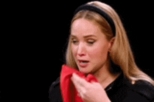 a woman is holding a red napkin in her hand and blowing her nose .