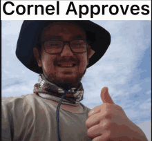 a man wearing a hat and scarf gives a thumbs up in front of a cornell approves banner