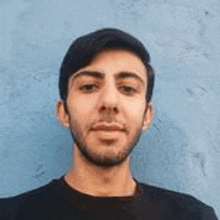 a man with a beard is standing in front of a blue wall and taking a selfie .