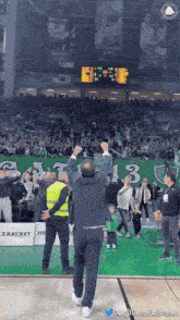 a man stands in front of a crowd at a basketball game with a scoreboard behind him that shows the time as 12:38