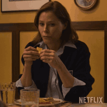 a woman sits at a table with a plate of food and a glass of water with netflix written on the table