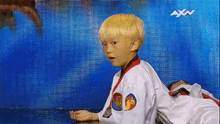 a young boy in a taekwondo uniform is standing in front of a blue wall with axn written on it