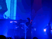 a man sings into a microphone while a drummer plays drums