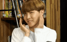 a young man in a white shirt is making a funny face in front of a bookshelf filled with books .