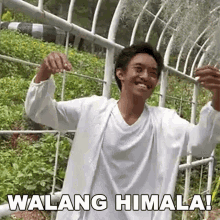 a man in a white shirt is standing in front of a greenhouse and smiling while holding a plant .