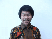 a man wearing glasses and a floral shirt smiles at the camera