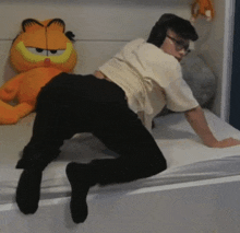 a person kneeling on a bed next to a stuffed garfield cat