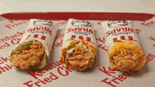 three kentucky fried chicken wraps are sitting on a tray