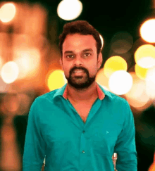 a man with a beard wearing a blue shirt stands in front of a blurry background