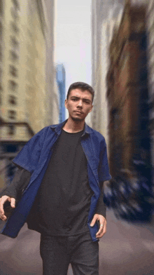 a man in a blue shirt and black t-shirt stands in a city street