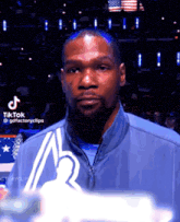 a man with a beard and a blue jacket is standing in front of an american flag .